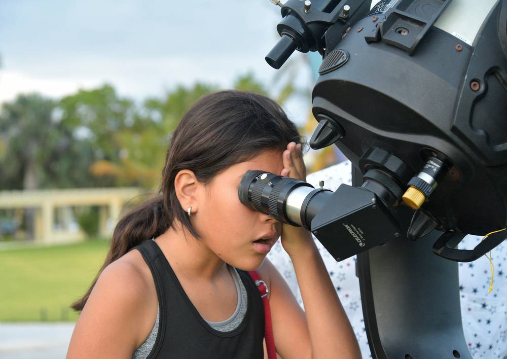 Una niña mira concentrada por el ocular de un telescopio de día